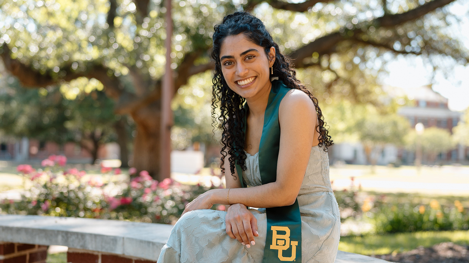 Girl on bench smiling with graduate clothing