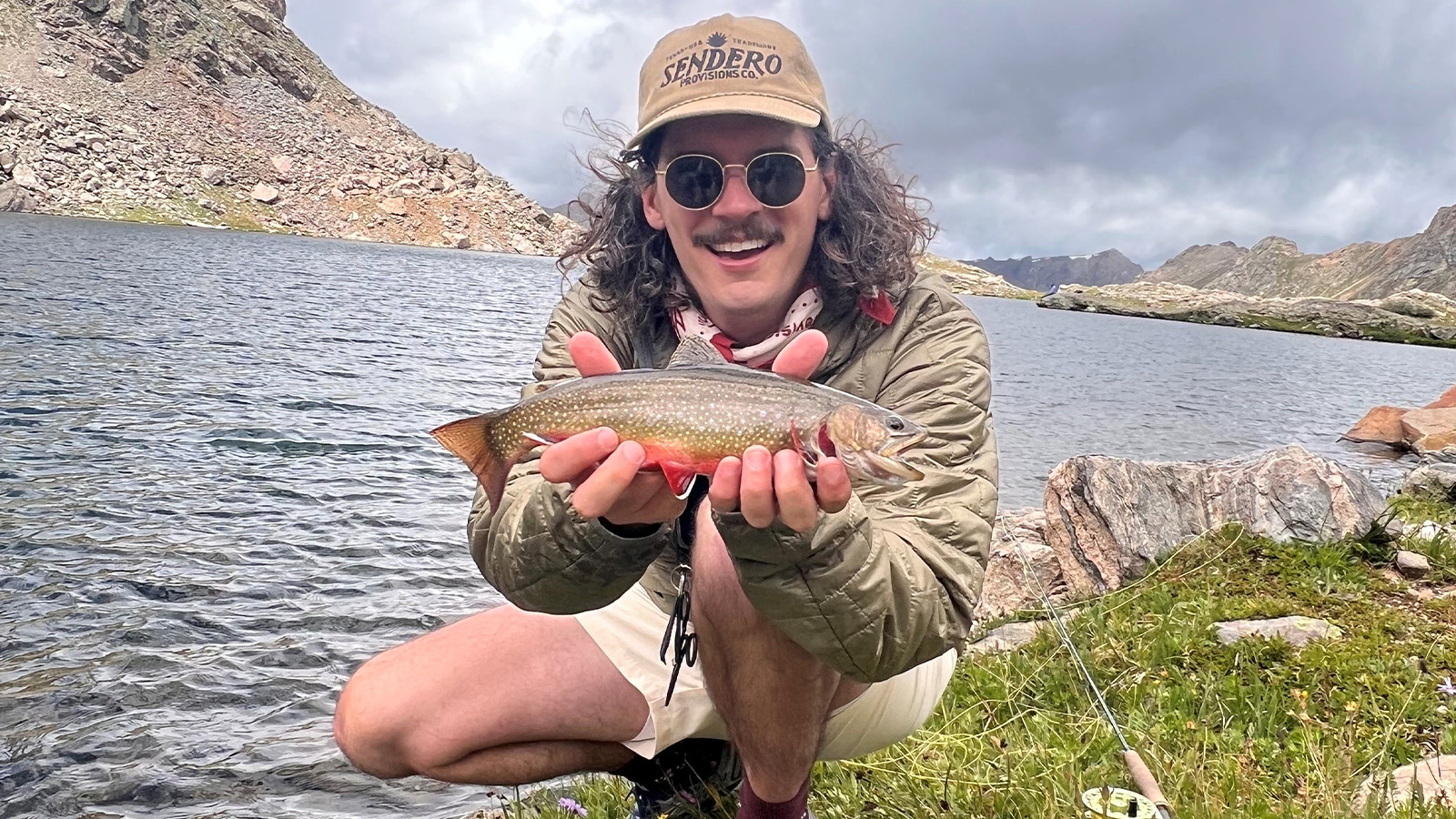 Dylan Washington holds a fish by a river.