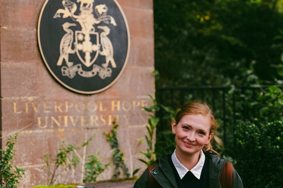 Emma Fenske smiles at the camera while standing in front of University of Liverpool's sign.