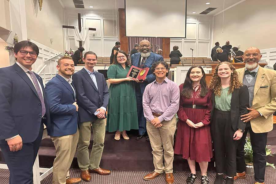 Male and female student presenters smile at camera with department chair and pastor