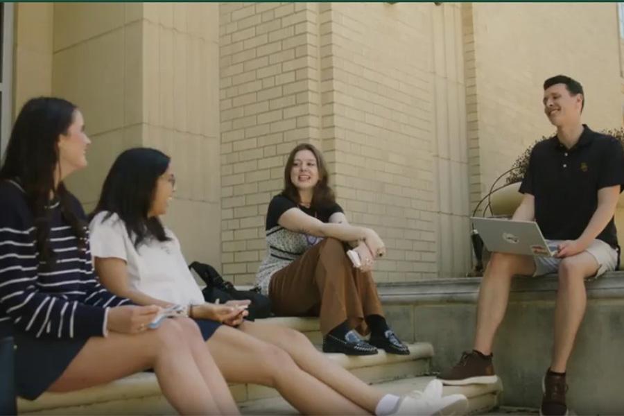 Three female students and on male student sit on the steps of Tidwell building laughing and talking.