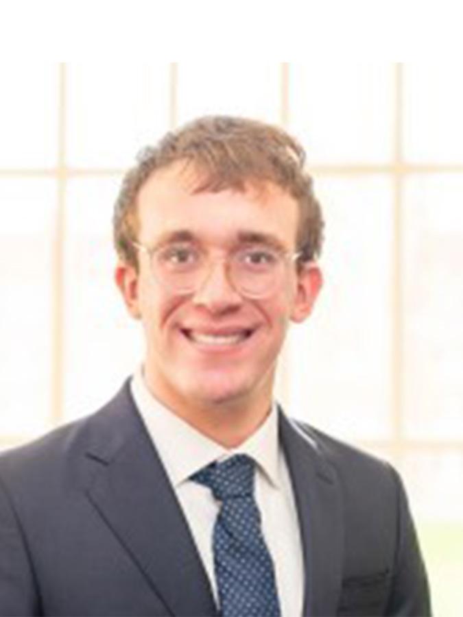 Philip Chivily wears a suit and glasses and smiles at the camera