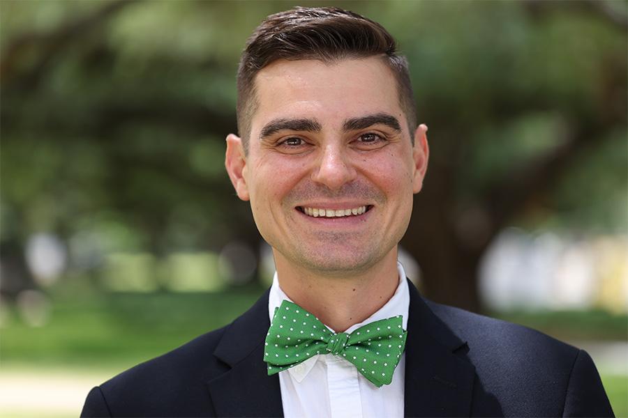 Dr. Daniel Watkins wears a suit and green bow tie and faces the camera smiling