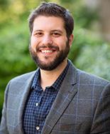 Dr. Anthony Gaspar a wears a grey suit and faces the camera smiling