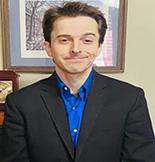 Dr. Andrew Gutkowski wears a black suit and faces the camera smiling