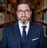 Dr.Benjamin Pietrenka wears a navy suit and faces the camera smiling