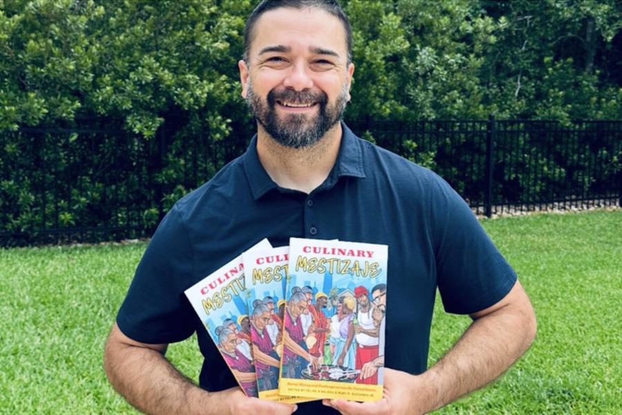 Dr. Felipe Hinojosa stands in a grassy yard holding three copies of his book and smiling