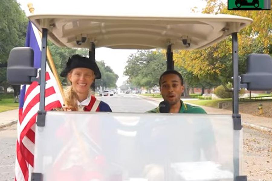 Dr. Sweet wears American Revolution military dress and sits in a gold cart with a male driver
