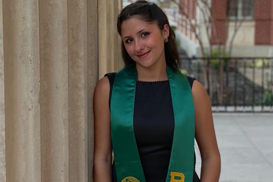 Irene Salandra wears her black, green and gold Baylor graduation robes and smiles at the camera.