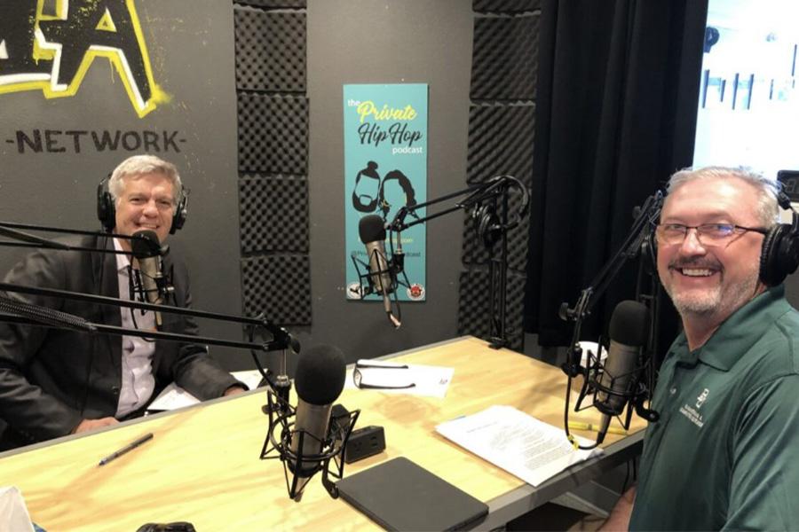 Dr. Sloan and Rick Tullis sit in a recording booth wearing headphones and smiling