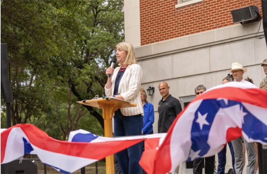 Baylor's President Linda Livingstone stands at a podium holding a microphone
