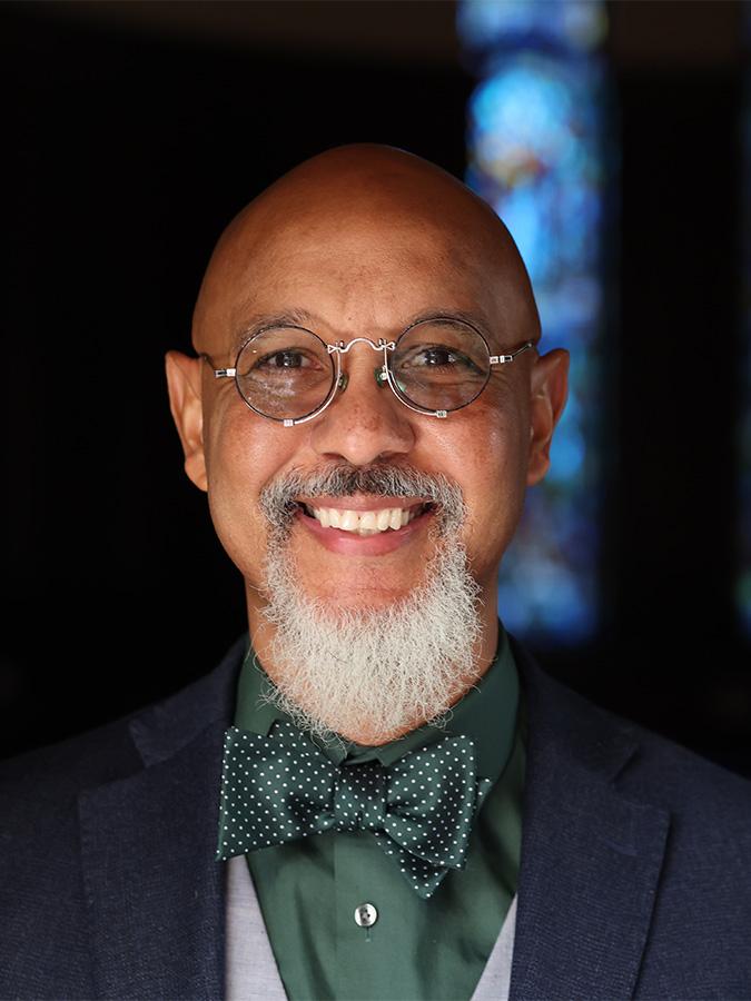 Man with stained glass behind him wearing glasses and smiling