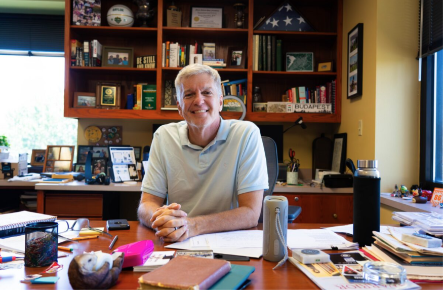 Dr. Sloan sits at his desk and smiles at the camera
